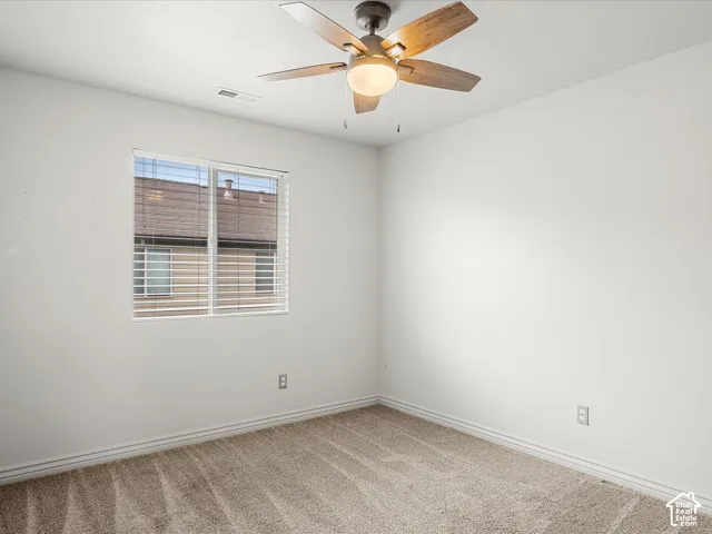 Carpeted room featuring a ceiling fan with light fixture, window with horizontal blinds, and white baseboard trim