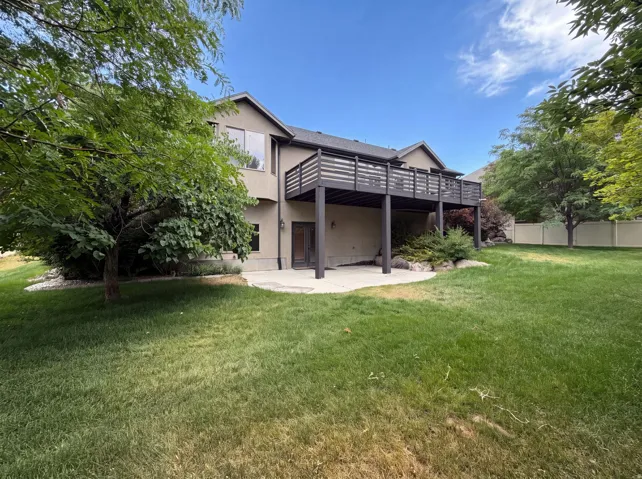 Expansive rear yard featuring a large concrete patio, a second-story deck with dark wood railing, and established trees