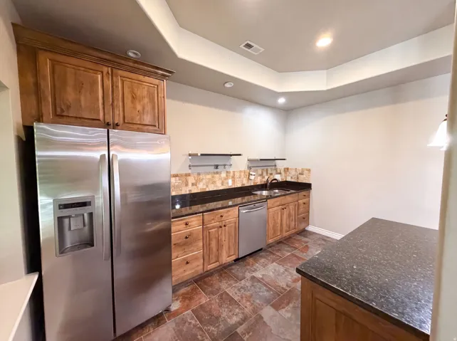 Kitchenette featuring wood cabinetry, stainless steel appliances, dark stone countertops, and a tiled backsplash