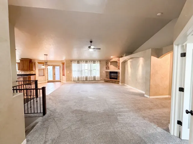 Spacious living area featuring vaulted ceilings, a stone-accented fireplace, and a ceiling fan