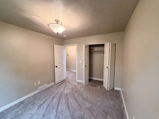 Carpeted room featuring a double-door closet with shelving, neutral wall paint, white baseboards, and a decorative ceiling light fixture