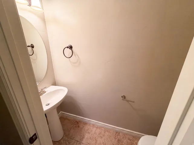 Pedestal sink with a polished chrome faucet, an oval mirror, and a bronze-finish towel ring