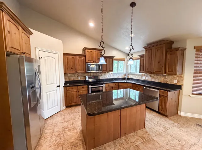Kitchen featuring a central island with a dark countertop, extensive wood cabinetry, stainless steel appliances, and tile flooring