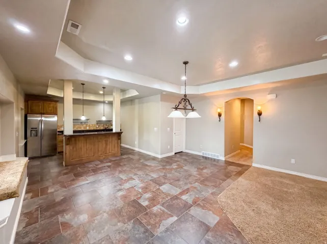 Spacious open-concept area featuring multi-toned tile flooring, recessed lighting, and a kitchen bar with pendant lighting and stainless steel appliances