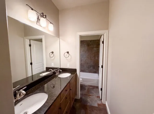 Double vanity with dark granite-finish countertop, undermount sinks, and wood-finish cabinetry