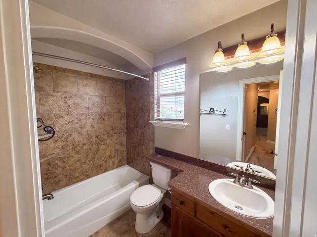 Bathroom featuring a wood-finish vanity with an integrated sink, a large wall-mounted mirror, and a three-light fixture