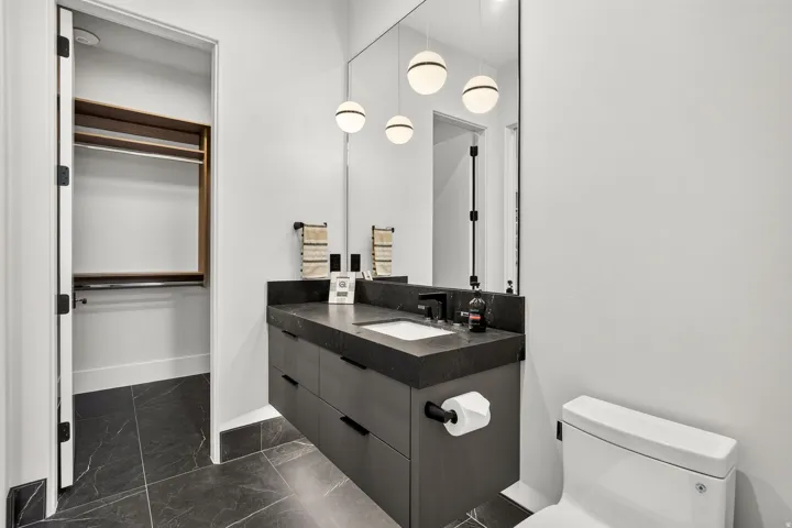 Bathroom vanity with a dark countertop and integrated sink, under-mount cabinetry, and a full-height mirror