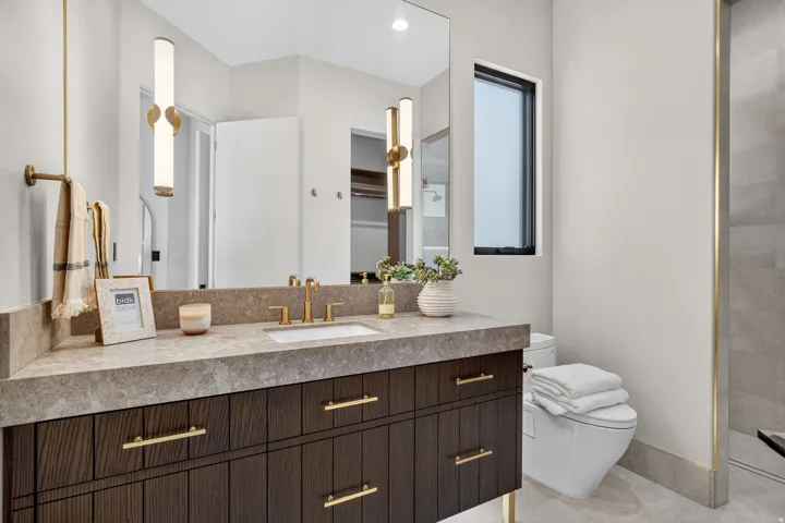 Dark wood vanity with gold-tone hardware, rectangular undermount sink, and a stone-finish countertop