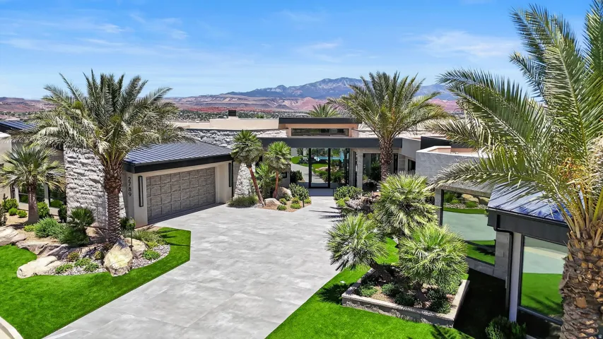 Modern architectural residence featuring extensive stone veneer, expansive glass walls, a textured garage door, a concrete driveway, and mature palm trees