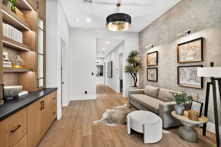 Hallway featuring wood-finish flooring, built-in shelving with integrated lighting, a textured accent wall, and a contemporary ceiling fixture