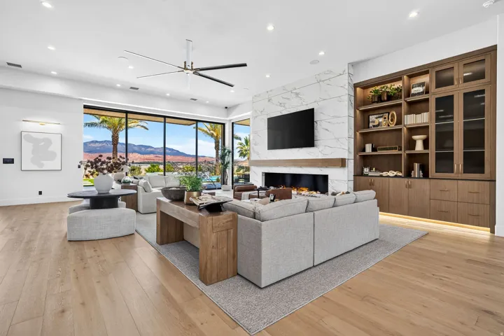 Spacious living area featuring expansive floor-to-ceiling windows, a modern linear fireplace with a stone surround, wood-finish flooring, recessed lighting, and custom built-in cabinetry with integrated lighting