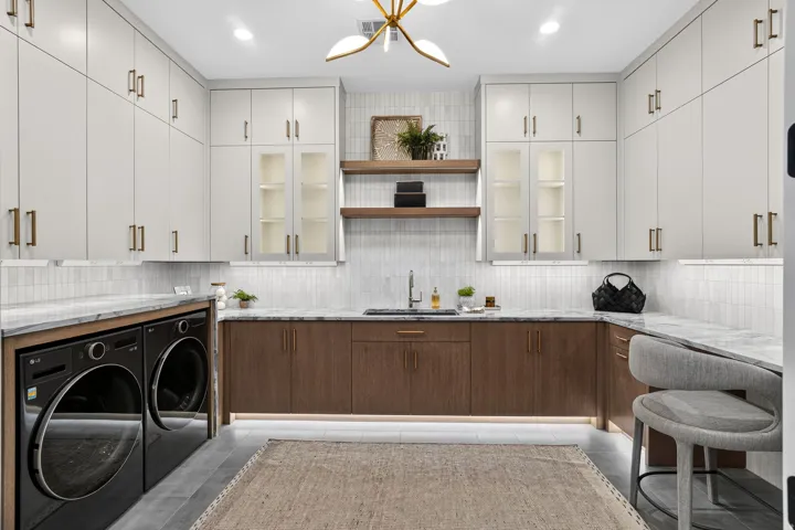 Laundry room featuring extensive upper and lower cabinetry, integrated washer and dryer units, a utility sink, and stone countertops