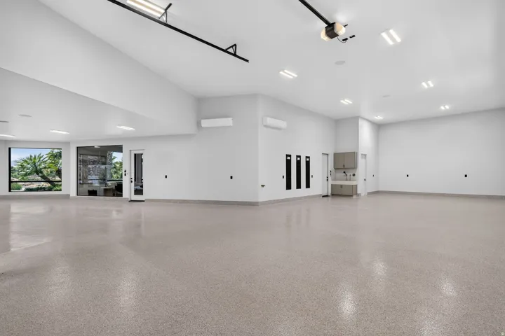 Spacious garage featuring high ceilings, epoxy flooring, large windows, recessed lighting, and built-in cabinetry with a utility sink