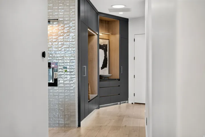 Hallway featuring wood-finish flooring, recessed lighting, and a built-in cabinetry system with dark flat-panel doors and light wood-paneled interior accents