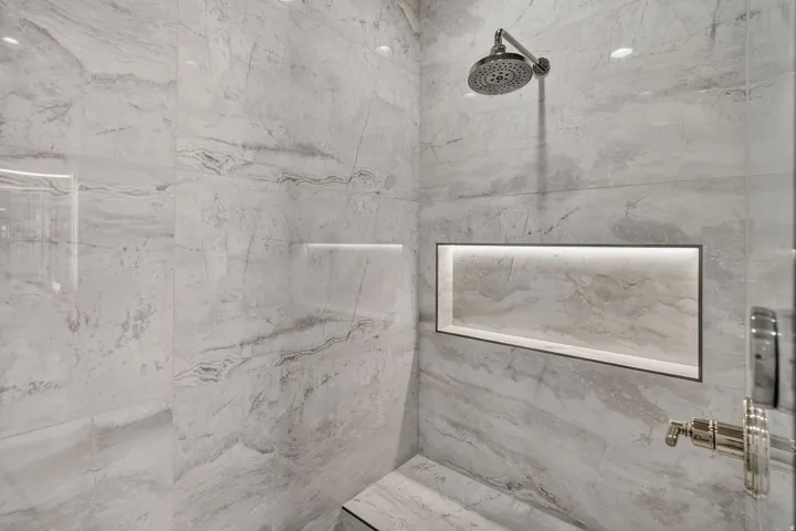Shower featuring large format marble-look tile, a built-in bench, a recessed niche with integrated lighting, a rainfall showerhead, and polished nickel fixtures