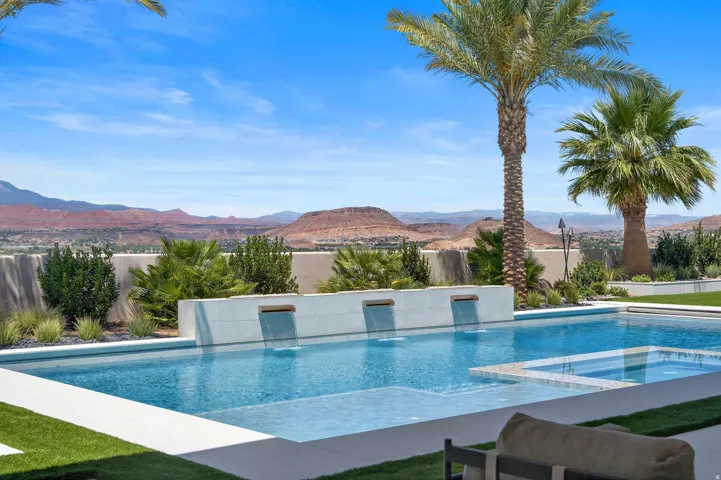 Outdoor entertaining area featuring a rectangular pool with integrated spa, multiple water features, and a surrounding artificial turf patio