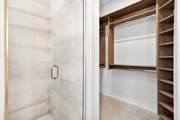 Glass shower enclosure with brass-finish framing and handle, alongside a walk-in closet featuring wood-finish shelving and hanging rods