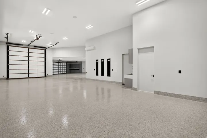 Spacious garage featuring a durable epoxy floor, multiple overhead sectional doors with translucent panels, and extensive overhead lighting