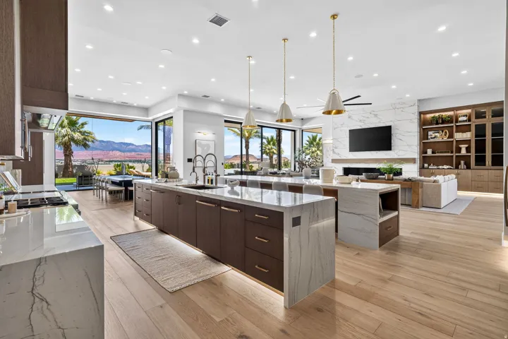 Spacious open-concept living area featuring a gourmet kitchen with waterfall island, wood-finish flooring, a contemporary fireplace with a large format tile surround, and full-height built-in shelving