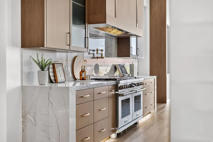 Gourmet kitchen featuring a stainless steel professional range, a pot filler faucet, stone countertops with waterfall edge, and custom cabinetry with varied finishes