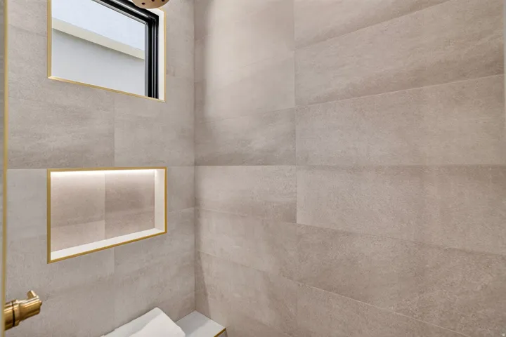 Tiled shower enclosure featuring a built-in bench, integrated niche with accent lighting, a window with golden trim, and a gold-toned shower fixture