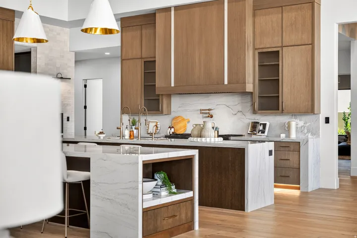 Gourmet kitchen featuring a waterfall island, wood-finish cabinetry, integrated appliances, and a full-height stone backsplash