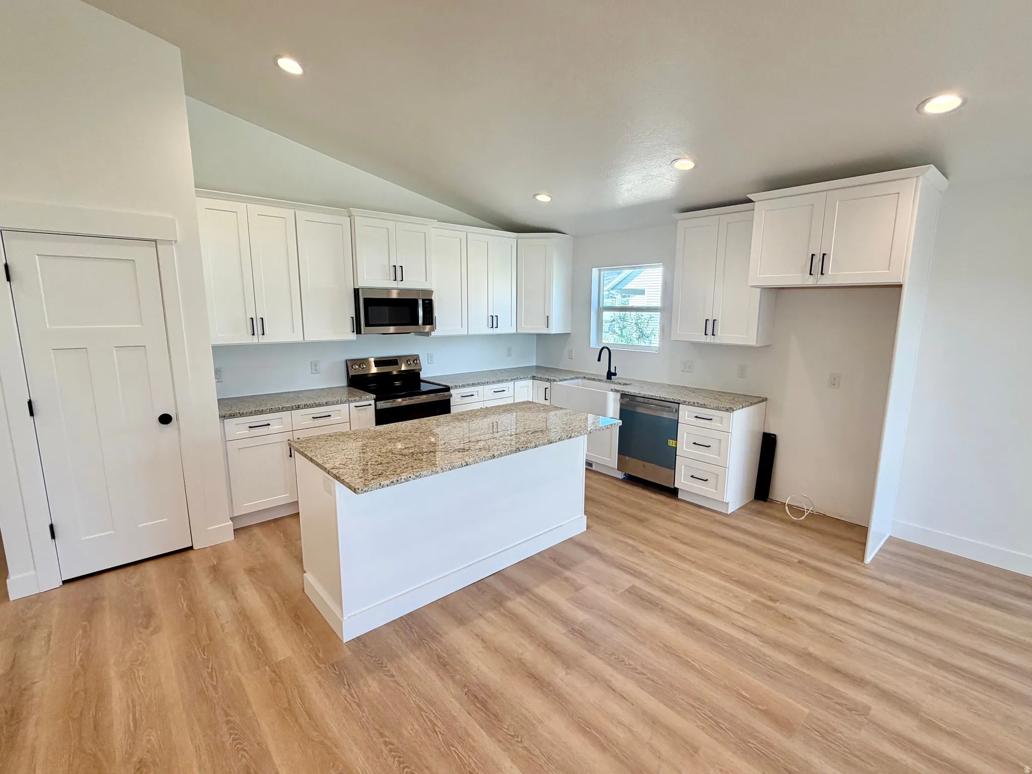 Modern kitchen featuring a central island with granite countertop, white shaker cabinetry with dark hardware, recessed lighting, and wood-finish flooring