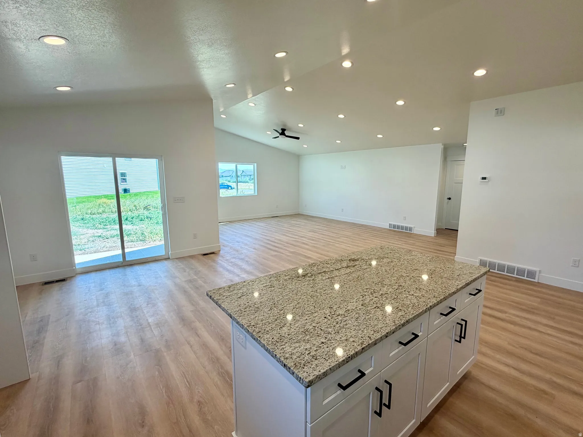 Kitchen island featuring a light-toned granite countertop and white cabinetry with black hardware