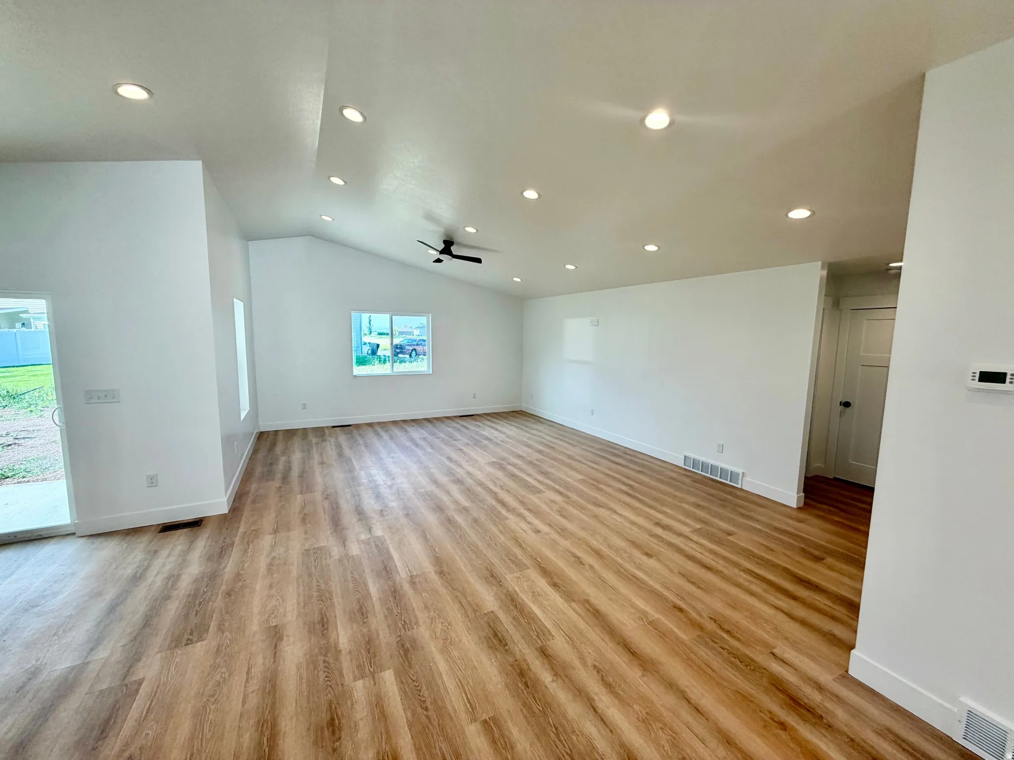Spacious room featuring vaulted ceilings, recessed lighting, wood-finish flooring, a ceiling fan, and a sliding glass door to the exterior