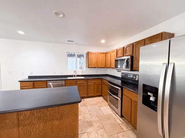 Kitchen featuring light wood cabinetry, dark countertops, and stainless steel appliances