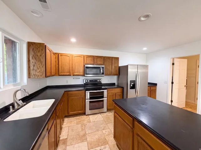 Kitchen featuring wood cabinetry, dark countertops, a double basin sink, stainless steel appliances, and tile flooring