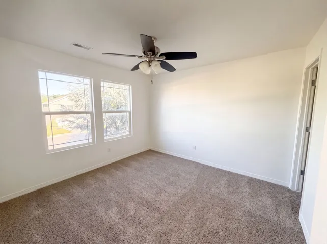 Carpeted room with a ceiling fan, two windows, and white walls