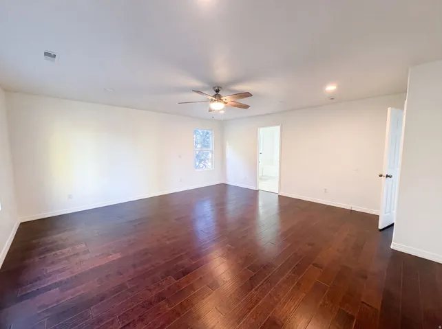 Spacious interior room featuring rich wood-finish flooring, recessed lighting, a ceiling fan with light fixture, white baseboards, and a window