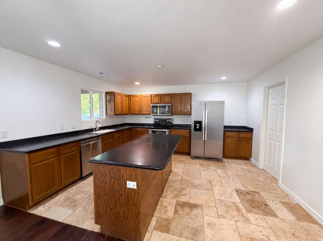 Kitchen featuring a central island, wood cabinetry, dark countertops, and stainless steel appliances
