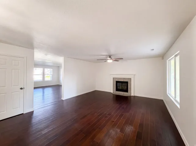 Spacious room featuring rich wood-finish flooring, a ceiling fan, and a fireplace with a light-toned mantel and tile surround