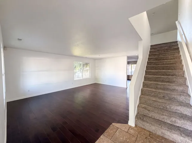 Open-concept living area featuring dark wood-finish flooring, white walls, and multiple windows