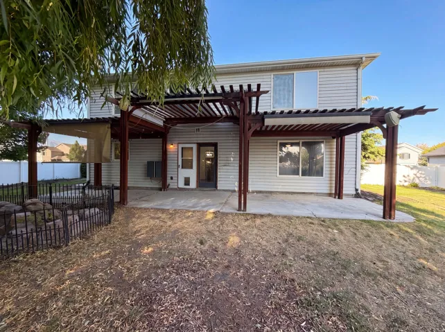 Rear exterior featuring a pergola-covered patio, light-colored siding, and white vinyl fencing