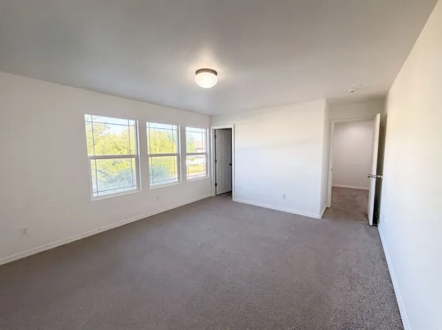 Spacious room featuring three large windows, neutral gray carpeting, and white painted walls