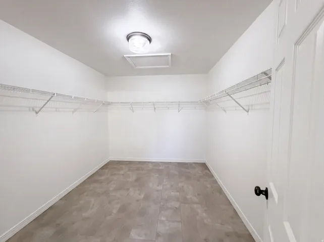 Spacious closet featuring wood-finish flooring, white wire shelving, baseboard trim, and a ceiling-mounted light fixture