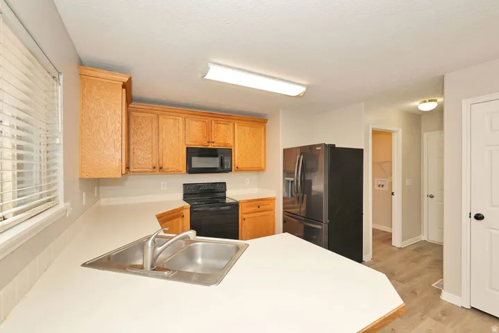 Kitchen featuring wood cabinetry, light countertops, and black appliances