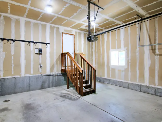 Concrete flooring garage featuring a wooden staircase, overhead garage door opener, and interior access door