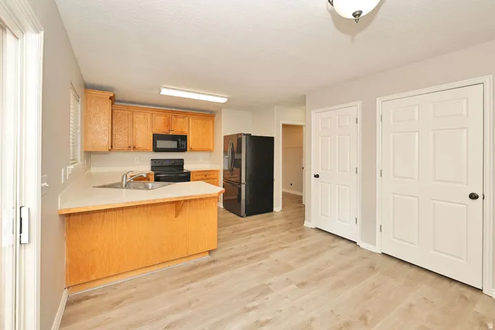 Kitchen featuring wood cabinetry, black appliances, light-toned countertops, and wood-finish flooring