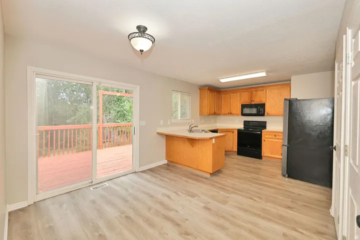 Kitchen and dining area featuring wood-finish flooring, a full kitchen appliance suite in black, light wood cabinetry, and a peninsula with an integrated sink