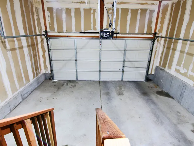 Garage featuring a white sectional door, concrete flooring, exposed wall studs, and concrete foundation walls