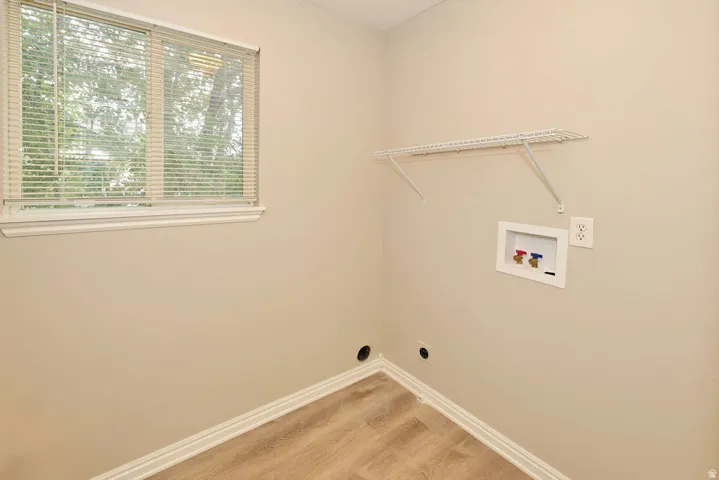 Laundry area featuring wood-finish flooring, a window with blinds, a wire shelving unit, and plumbing hookups