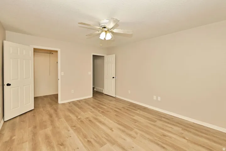 Spacious room featuring wood-finish flooring, light-toned walls, and a ceiling fan with integrated lighting