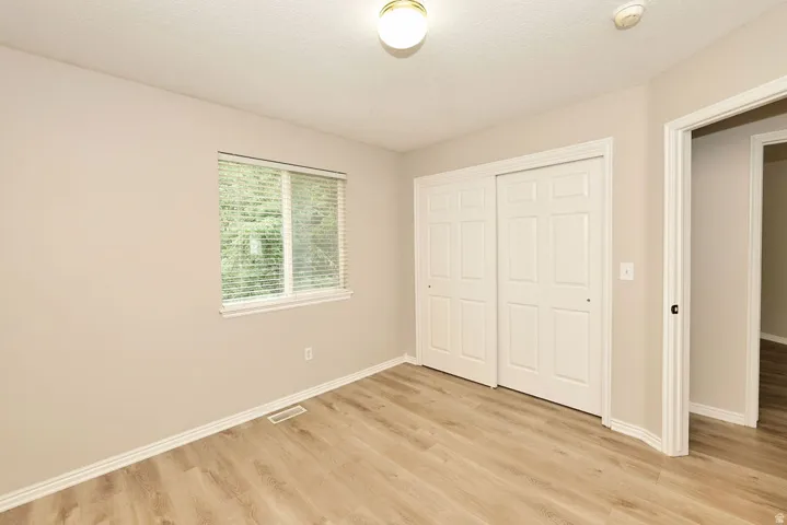 Spacious room featuring wood-finish flooring, neutral-toned walls, a window with blinds, and a built-in closet with sliding doors