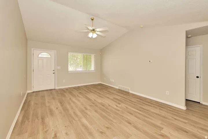 Spacious living area featuring wood-finish flooring, vaulted ceilings, and a ceiling fan with integrated lighting