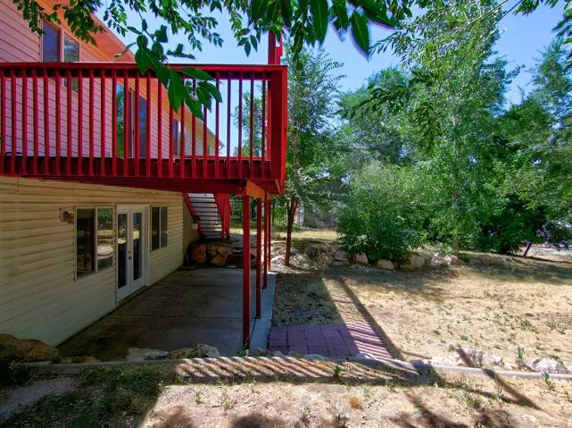 Expansive outdoor space featuring a concrete patio, red deck, and mature trees providing natural shade