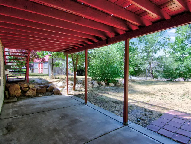 Covered concrete patio featuring a red-stained wood ceiling, structural posts, and a red-stained wood staircase